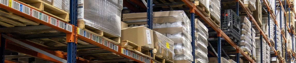 View down a fully stocked warehouse storage aisle with pallet racking.