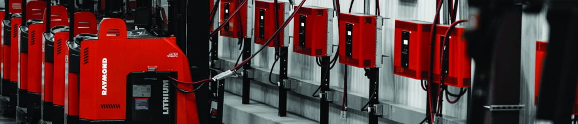 Raymond electric forklifts connected to warehouse wall-mounted charging stations.
