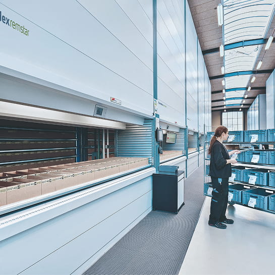Warehouse worker reviewing inventory totes beside a vertical lift module.
