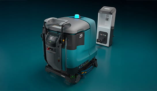 Tennant autonomous floor scrubber docked at a charging station in a warehouse facility.