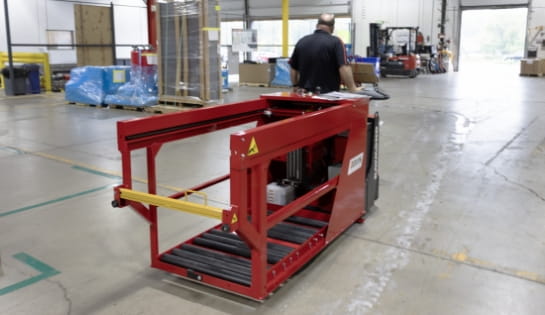 Warehouse worker utilizing a pallet jack with an attached battery extractor in a loading dock area.