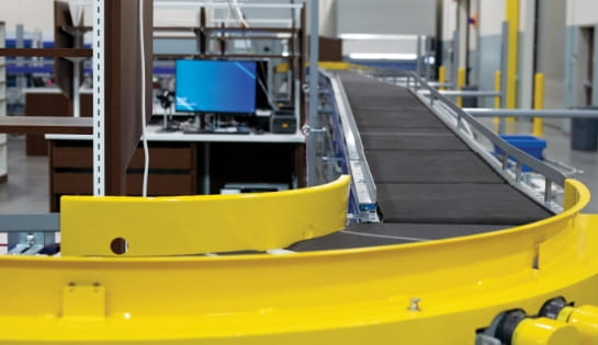 Curving belt conveyor system integrated with a computerized control station in a warehouse.