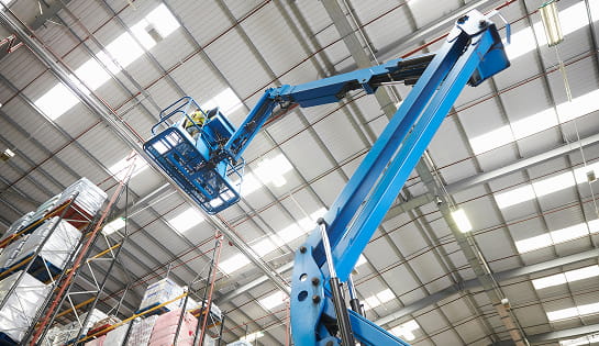 Extended boom lift operating within a high-bay warehouse facility.
