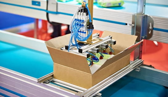Automated case packing robot arm placing product into a shipping box on an assembly line.