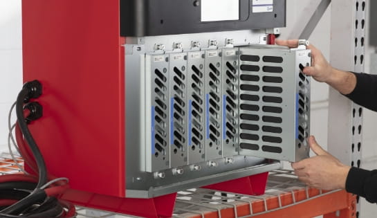 Technician sliding a modular component out of an industrial forklift battery charger on a storage rack.