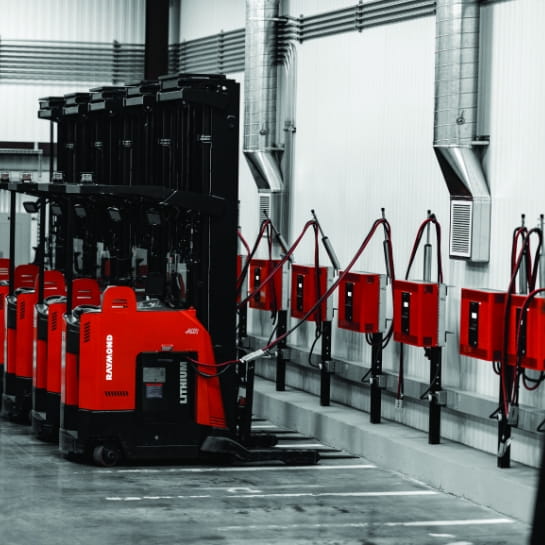 Raymond forklifts parked in a warehouse at industrial charging stations.