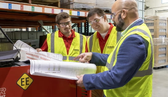 RSC engineers reviewing facility blueprints with a customer on a warehouse floor.