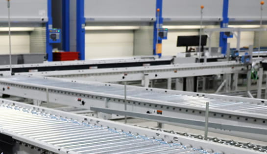 Automated conveyor system running in front of picking stations and vertical lift modules in a distribution center.