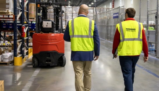 RSC team member walking a warehouse site with a customer past pallet racking and a Raymond forklift.