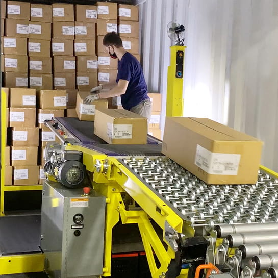 Warehouse worker unloading cartons from a trailer onto a Destuff-It portable conveyor system