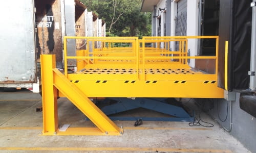 Yellow dock lift bridging the gap between a truck trailer and a warehouse dock door.