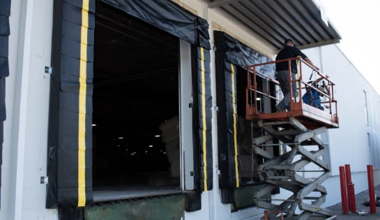 Technicians on a scissor lift installing a warehouse loading dock door.