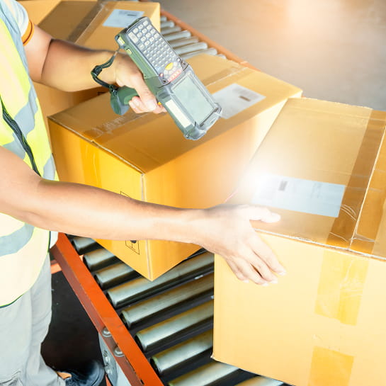 Warehouse worker wearing a safety vest scanning a package on a conveyor belt.