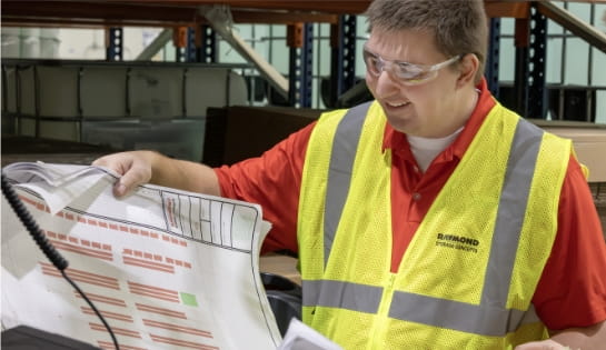 Raymond Storage Concepts engineer in a safety vest holding a warehouse racking project blueprint