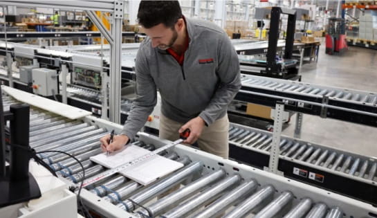Raymond Storage Concepts engineer measuring a conveyor section and taking notes in a warehouse.