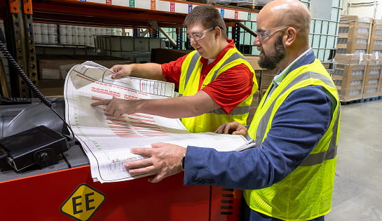 Raymond Storage Concepts engineer and operations manager reviewing a racking layout blueprint next to a forklift