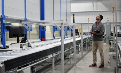 Raymond Storage Concepts sales engineer observing an AS/RS and conveyor system while taking notes.