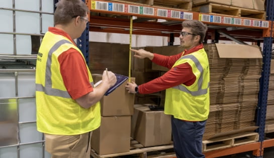 Raymond Storage Concepts engineer measuring pallet and racking spacing while another engineer records the measurements