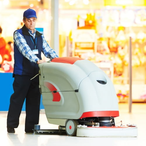 Worker wearing a safety vest operating a floor scrubber in a retail space