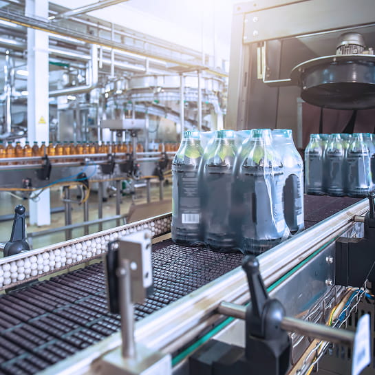 Beverage bottles moving on a conveyor belt after exiting a shrink wrapper in a bottling plant.