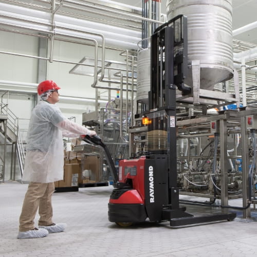 Worker in sanitary PPE gear pushing a walkie stacker in a food processing plant