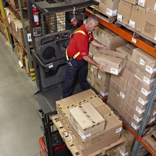 Operator tethered to a Raymond orderpicker picking boxes from warehouse racking onto a pallet.