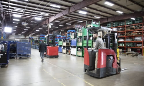 Raymond counterbalanced forklift crossing a marked pedestrian walkway in a warehouse facility.