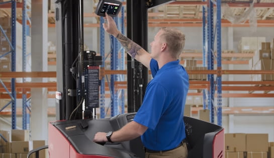 Forklift driver interacting with an iWAREHOUSE monitor screen mounted on a Raymond forklift