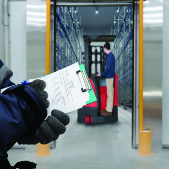 Raymond forklift entering a warehouse freezer room with a gloved hand holding a clipboard in the foreground