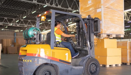 LP gas-powered forklift lifting a wrapped pallet of boxes in a warehouse staging area