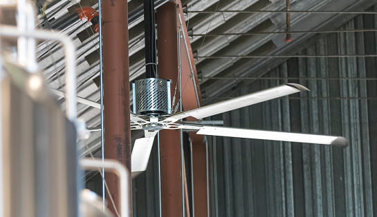 Industrial fan mounted between ceiling rafters in a large warehouse