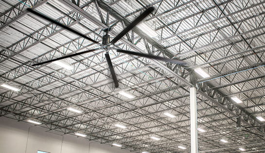 Low-angle view of an industrial ceiling fan surrounded by warehouse rafters