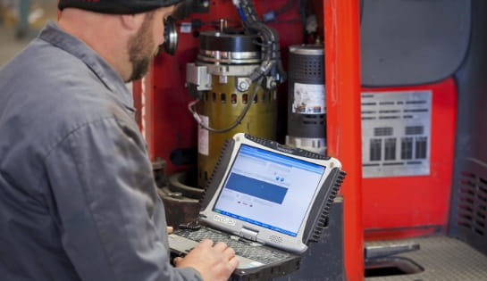 Technician reviewing repair history on the iWAREHOUSE asset maintenance manager interface in front of a forklift engine