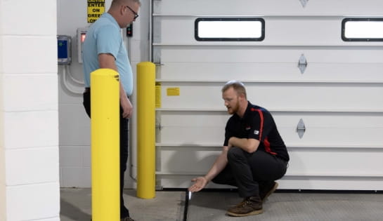 Dock and door specialist pointing out a dock leveler misalignment to a customer in a warehouse