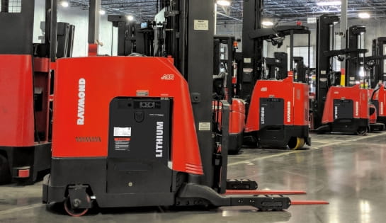 Several standing Raymond counterbalanced forklifts powered by lithium-ion batteries operating in a warehouse
