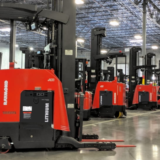 Several standing Raymond counterbalanced forklifts powered by lithium-ion batteries operating in a warehouse