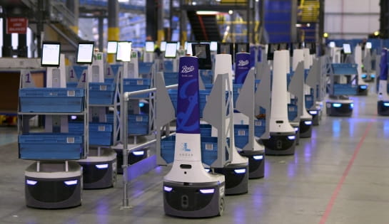 White and blue Locus autonomous mobile robots (AMRs) delivering orders to workers in a warehouse