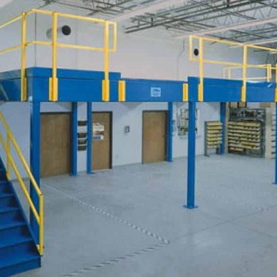 Blue industrial mezzanine with yellow safety railings installed above office doors in a warehouse