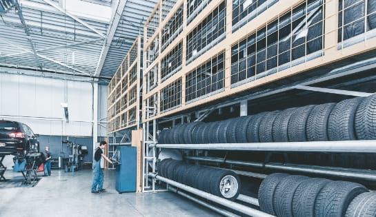 Male worker operating the controls for a Kardex oversize AS/RS storing vehicle tires inside an auto shop