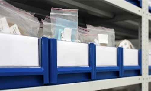 Blue labeled bins containing small parts bags organized neatly on a cabinet shelf