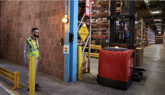 Warehouse pedestrian wearing a safety vest stopped at a doorway as an automated forklift drives past