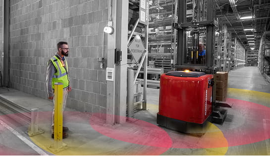 Warehouse worker walking toward a passageway near a forklift with floor projections indicating safety sensing technology