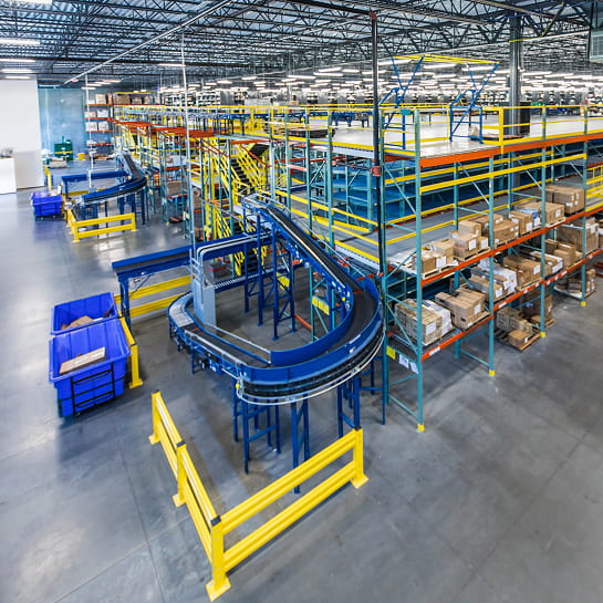 Multi-level yellow and blue pick module in a warehouse featuring integrated conveyors moving between levels and cartons stored on each tier for order picking