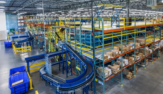Multi-level yellow and blue pick module in a warehouse featuring integrated conveyors moving between levels and cartons stored on each tier for order picking