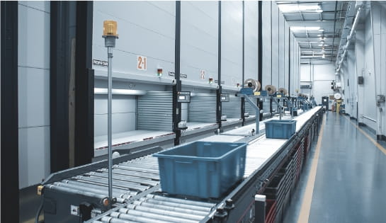 Totes rolling down a conveyor line for an order picker positioned in front of multiple Kardex vertical lift modules in a warehouse