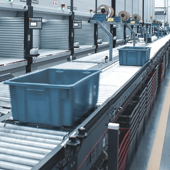 Totes rolling down a conveyor line for an order picker positioned in front of multiple Kardex vertical lift modules in a warehouse