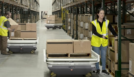 Warehouse worker picking orders and placing them on a Locus robotics autonomous mobile robot with a pallet in a warehouse aisle