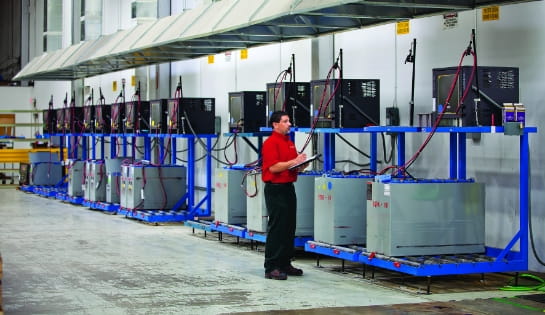 Raymond Storage Concepts energy specialist holding a clipboard and reviewing a line of industrial power systems mounted on a warehouse wall
