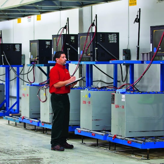 Raymond Storage Concepts energy specialist holding a clipboard and reviewing a line of industrial power systems mounted on a warehouse wall