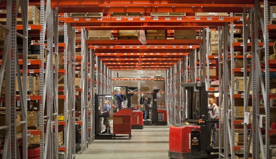 Warehouse aisle tunnel bay view showing Raymond lift trucks moving between racks while gathering orders